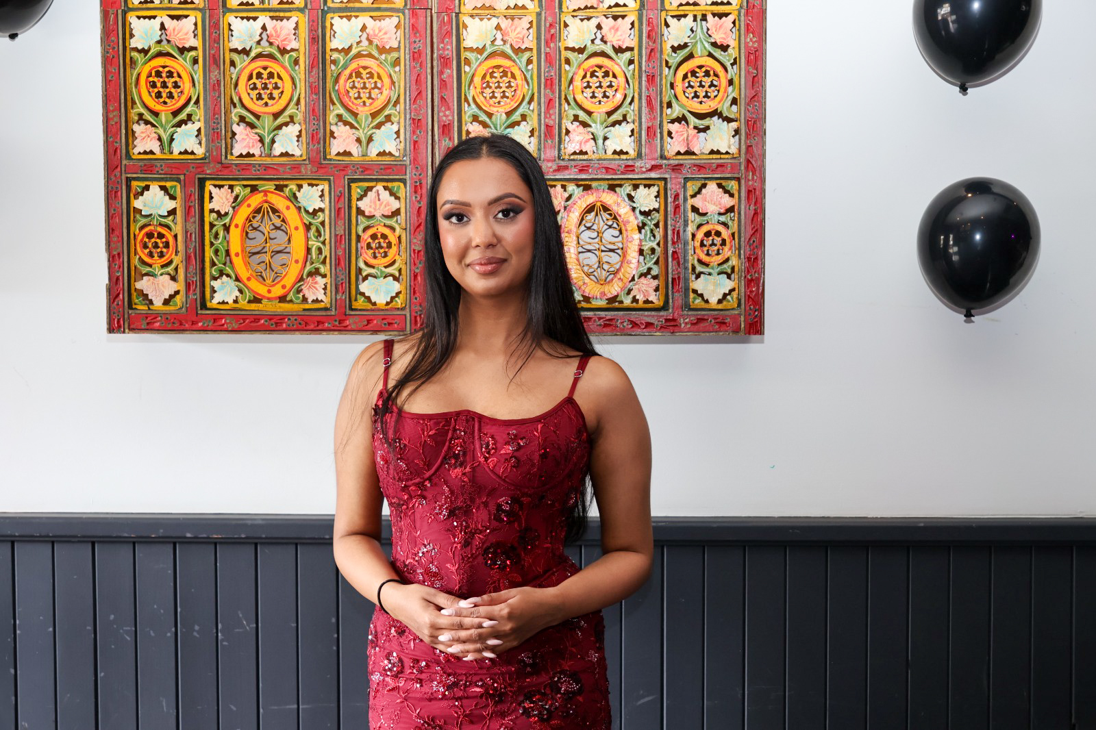 Guest in a red sequin dress in front of a carved painted wall panel