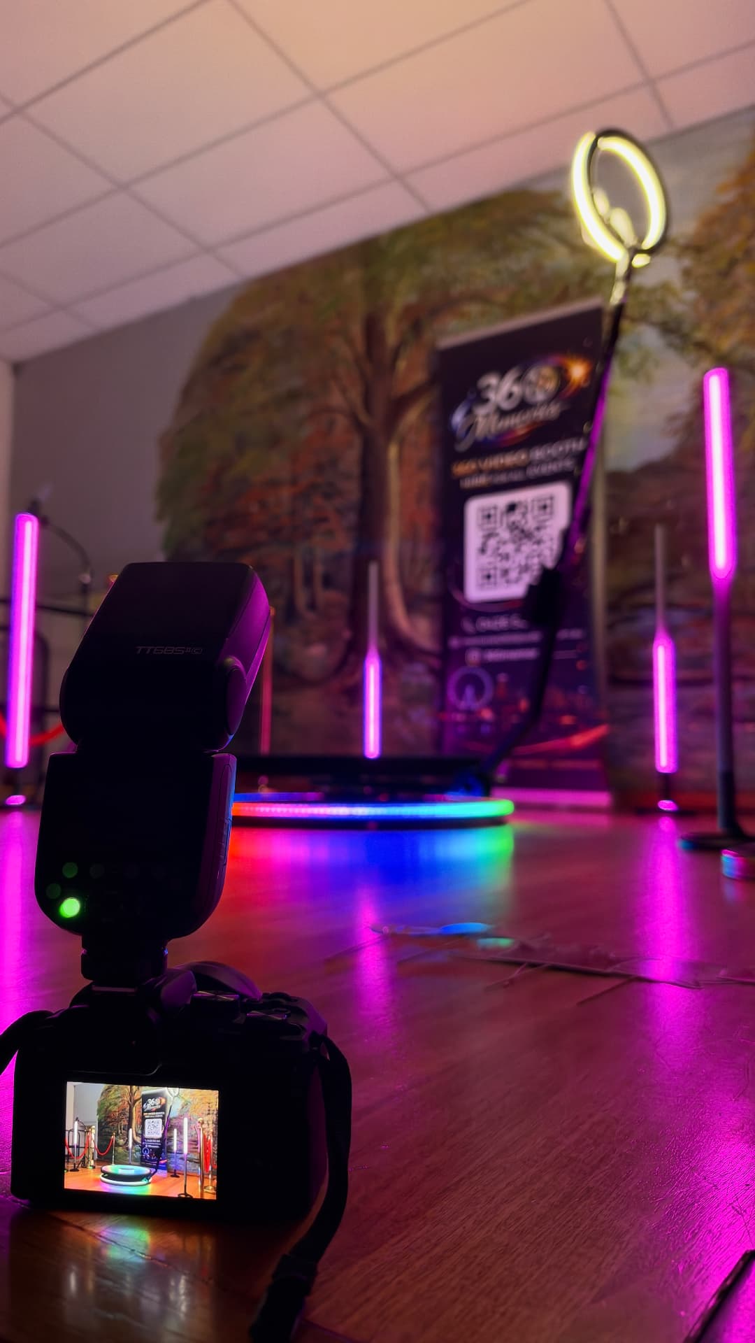Camera filming a 360 video booth setup with pink lights and a ring light