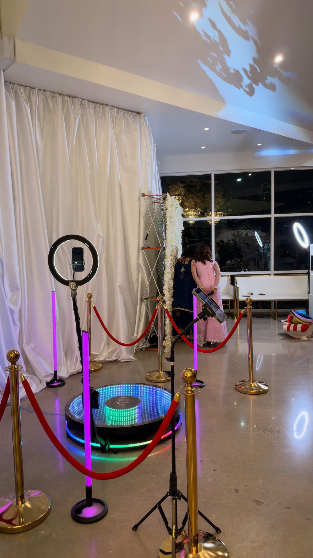 360 video booth with a ring light and gold stanchions beside white curtains