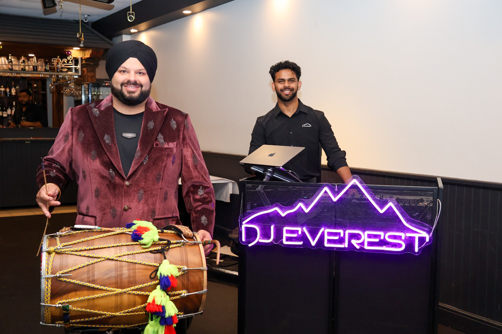 Dhol player and DJ posing beside the neon DJ booth