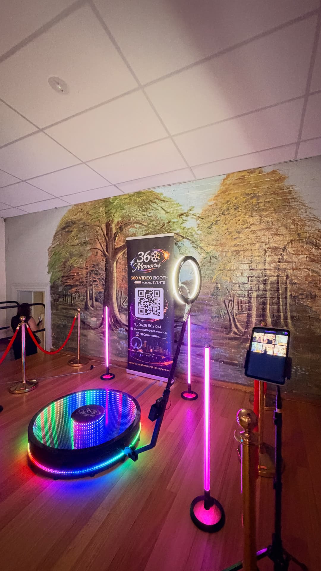 Colourfully illuminated 360 video booth in front of a woodland wall mural